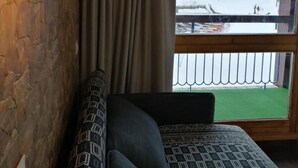 Una habitación con pared de madera, una lámpara colgante, una ventana con vista a un paisaje nevado y un sofá estampado.