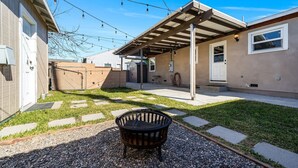 Ein Garten mit überdachter Terrasse, Feuerstelle und Kiesweg.