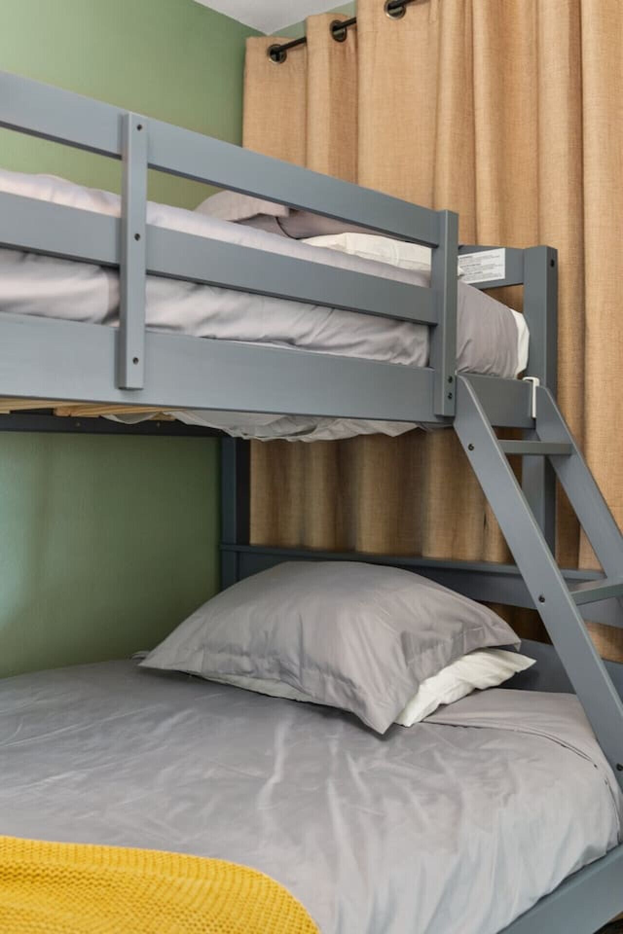 A bunk bed with a grey metal frame, a grey mattress, and a single pillow.