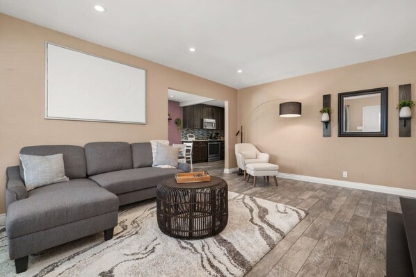 A modern living room with a grey sectional sofa, a round coffee table, and a patterned rug. - Newly Remodeled Home in the Heart of Orange County (Midway City)