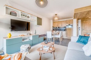 Una sala moderna con televisor de pantalla plana, un comedor con mesa y sillas, y una cocina con gabinetes de madera y horno empotrado.