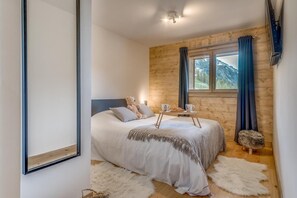A bedroom with a bed, a teddy bear, a tray with cups and a croissant, and a view of mountains through a window. - 200m from resort center, 3rd floor, view valley, swimming pool, sauna, hammam, balcony, tv (Tignes)