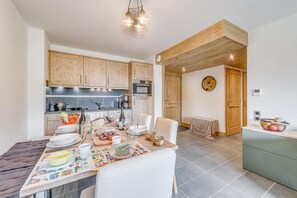 A modern kitchen with wooden cabinets, a dining table set for four, and a small side table with fruit.