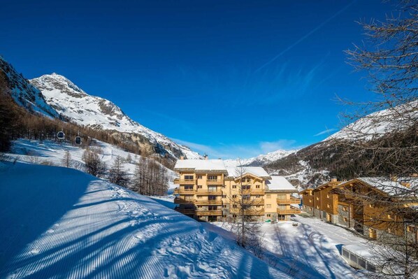 A snow-covered mountain landscape with a hotel featuring multiple balconies and a ski lift in the background.