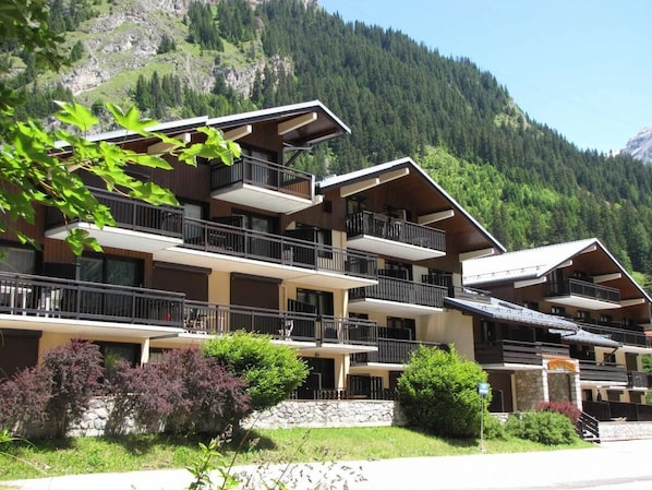 A multi-story hotel with balconies, set against a mountainous backdrop.