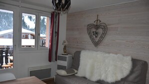 A cozy room with a grey sofa, a wooden table, and a view of a snowy landscape through a large window. - 1st floor, balcony, tv, ski locker, 21m², Pralognan-la-Vanoise (Pralognan-la-Vanoise)