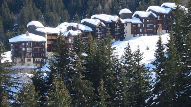 Una fila di edifici a più piani con tetti imbiancati dalla neve, circondati da fitti alberi sempreverdi.