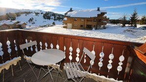 Um deck de madeira com mesa e cadeiras, com vista para uma paisagem nevada com edifícios e árvores.