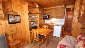 Interior de uma cabana de madeira com uma mesa de jantar, cadeiras, cozinha equipada com micro-ondas e frigorífico.