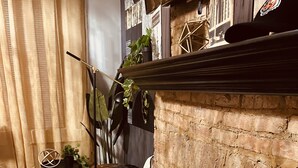 Une pièce chaleureuse avec une cheminée en briques, un plancher en bois et une petite table agrémentée d’une plante.