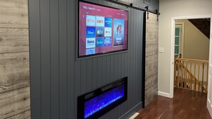 Un téléviseur fixé au mur, qui affiche différentes plateformes de diffusion en continu, et une cheminée située en dessous.