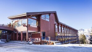 A modern wooden building with multiple windows and balconies, likely a hotel or lodge, with a clear view of snow-covered mountains in the background. - 100m from ski slopes, 6th floor, balcony, tv, 25m², Les Arcs (Les Arcs)