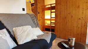 A dark blue sofa with a blanket and pillows, a small round table with a remote control, and a wooden bunk bed in the background. - 100m from ski slopes, 6th floor, balcony, tv, 25m², Les Arcs (Les Arcs)