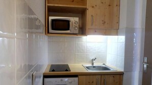 A compact kitchen with a microwave, dishwasher, and wooden cabinets. - 50m from ski slopes, 4th floor, view mountain, balcony, tv, 27m², Méribel-Mottaret (Méribel - Les Allues)