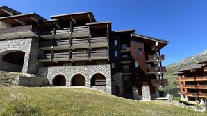 A multi-story hotel with stone arches, balconies, and a mountainous backdrop. - 50m from ski slopes, 4th floor, view mountain, balcony, tv, 27m², Méribel-Mottaret (Méribel - Les Allues)