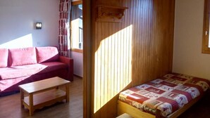 A small, cozy room with a wooden bunk bed, a red sofa, and a wooden table. - 50m from ski slopes, 4th floor, view mountain, balcony, tv, 27m², Méribel-Mottaret (Méribel - Les Allues)