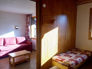 Ein kleiner, gemütlicher Raum mit einem Holzbett, einem roten Sofa und einem Holztisch.