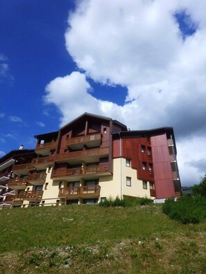 Un immeuble à plusieurs étages, doté de balcons, d’un toit en pente et d’un parterre gazonné.