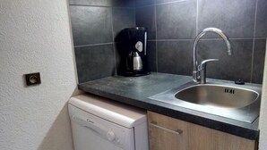 Cocina compacta con lavavajillas, cafetera y fregadero.
