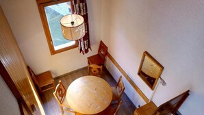 Un comedor con una mesa redonda de madera y cuatro sillas, una lámpara colgante y un ventanal con cortinas.