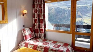 Una habitación acogedora con una cama, una mesa de madera y vistas a un paisaje montañoso a través de un ventanal grande.