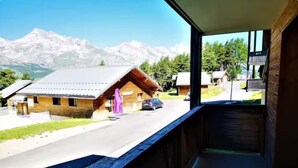 Une vue depuis un balcon donnant sur un paysage montagneux, avec des bâtiments en bois et une voiture garée dans la rue.