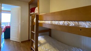 Une chambre avec un lit superposé, une échelle en bois, une porte blanche et une vue sur un balcon.