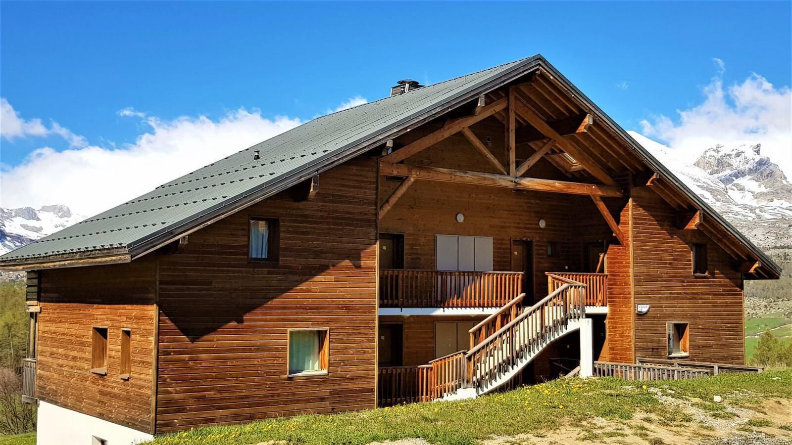 Eine Holzhütte mit Balkon und Treppe vor einer Berglandschaft.