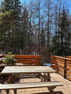 Eine Holzterrasse mit Picknicktischen und Bänken, umgeben von hohen Bäumen.