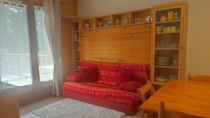 Une pièce chaleureuse avec un canapé rouge, une table à manger en bois et une bibliothèque remplie d’objets décoratifs.