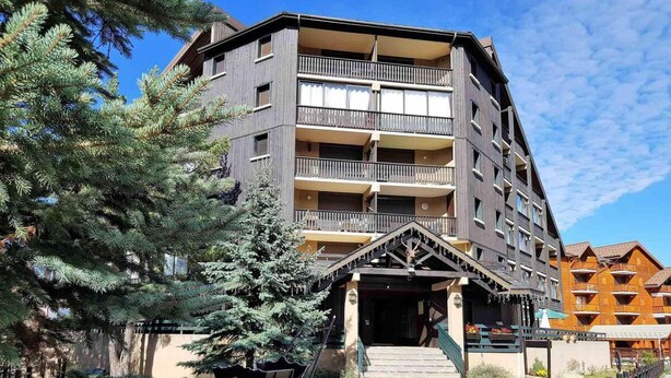 A multi-story hotel with a central entrance, balconies, and a surrounding wooden fence.