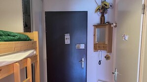 A small, cozy room with a bunk bed, a dark door, a small mirror, and a radiator.