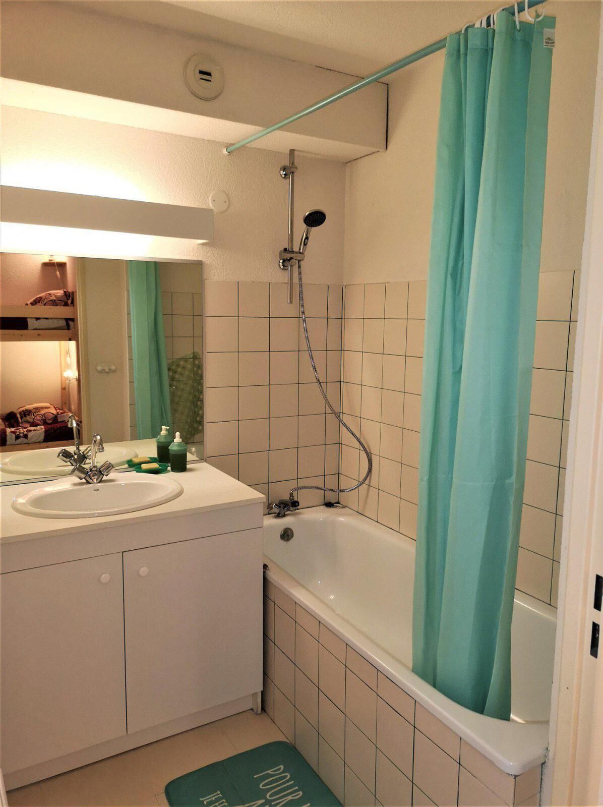 Een badkamer met een wastafel, spiegel, douche en een groen douchegordijn.