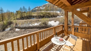 A wooden deck with a table and chairs, overlooking a mountainous landscape with a stone wall and trees. - 50m from ski slopes, 7th floor, swimming pool, sauna, hammam, balcony, tv, ski locker, 72m², Tignes (Tignes)