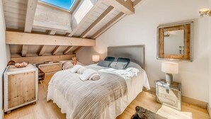 A bedroom with a skylight, wooden beams, a bed with pillows, a bedside table, a lamp, and a mirror. - 50m from ski slopes, 7th floor, swimming pool, sauna, hammam, balcony, tv, ski locker, 72m², Tignes (Tignes)