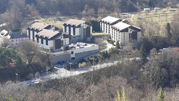 A modern building complex with multiple structures, surrounded by trees and open fields.