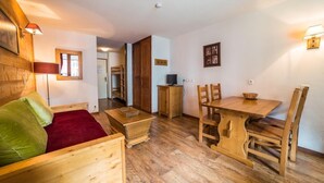 A cozy room with a wooden bed, a small wooden table, a dining table with chairs, and a television on a cabinet.