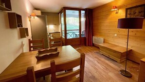 A wooden interior with a dining table, chairs, a bench, a floor lamp, and a view through a glass door to the outside.