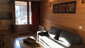 A cozy living room with a sofa, wooden walls, a dining table, and a view through a large window.