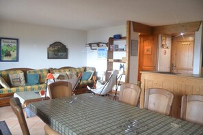 A cozy living room with a sofa, chairs, a dining table, and a kitchen area with wooden cabinets. - Ski-in/ski-out & foot of the slopes, 1st floor, view ski slopes, balcony, tv, ski locker, 65m² (Les Arcs)