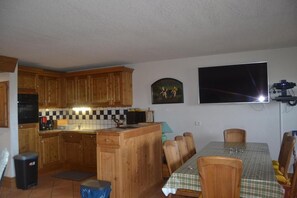 A kitchen with wooden cabinets, a tiled backsplash, a dining table with chairs, and a flat-screen TV mounted on the wall. - Ski-in/ski-out & foot of the slopes, 1st floor, view ski slopes, balcony, tv, ski locker, 65m² (Les Arcs)