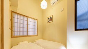 Habitación con dos camas, un celosía japonesa, una mesita de noche pequeña y una ventana con vistas.