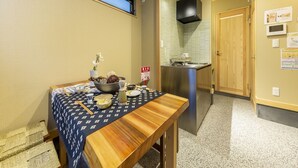 Una habitación compacta con una mesa de comedor lista para dos personas, una pequeña cocina y una ventana con persianas.