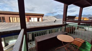 Terraza de madera con una mesa y sillas, con vistas a un paisaje montañoso.