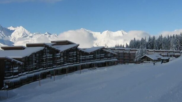 Una cabaña cubierta de nieve con varios edificios, con montañas nevadas al fondo.