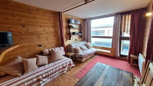 Interior acogedor de una cabaña con pared de madera, un sofá, una mesita y un televisor.