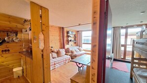 Interior acogedor de una cabaña con paredes de madera, kitchenette, zona de comedor y sofá.