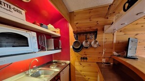 Cocina pequeña con pared roja, microondas, estufa y ollas colgantes.