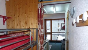 A narrow hallway with bunk beds on the left, a wooden wall, and a view of a balcony with outdoor furniture. - 100m from ski lifts, 6th floor, balcony, tv, 19m², Les Arcs (Les Arcs)