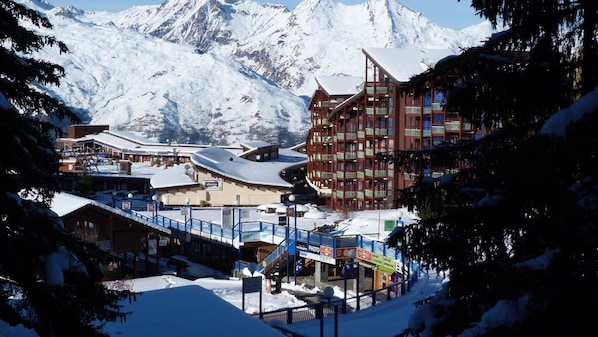 A snow-covered mountain town with a ski resort building, a Supermercado, and a blue pedestrian bridge.